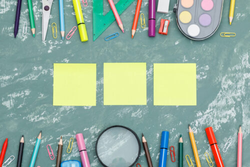 Back to school concept with sticky notes, magnifying glass, school supplies on plaster background flat lay.